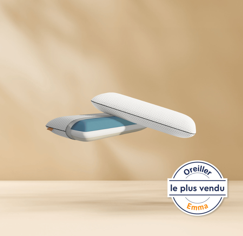 Deux coussins modernes avec une housse texturée blanche et une couche intérieure bleue flottent sur un fond beige. Un badge circulaire en français en bas à droite indique Oreiller le plus vendu Emma.