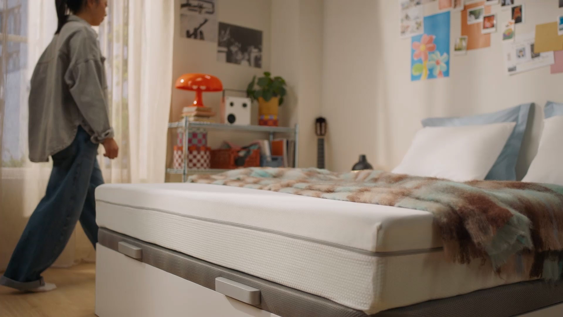 Person sitting on a bed with a white mattress in a bright bedroom.