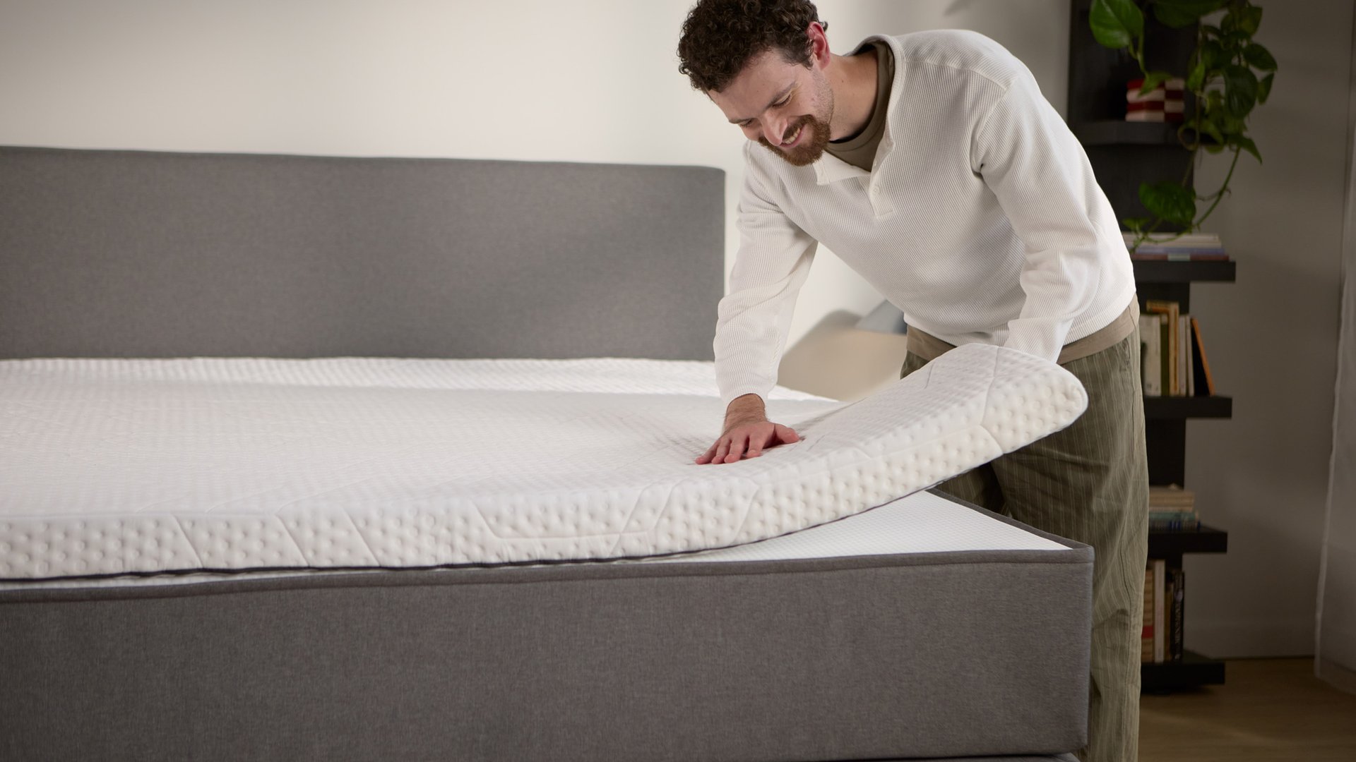 Detailansicht: Ein separater Matratzen-Topper wird auf dem Boxspringbett angehoben und zeigt die zusätzliche Polsterung an der Oberfläche.