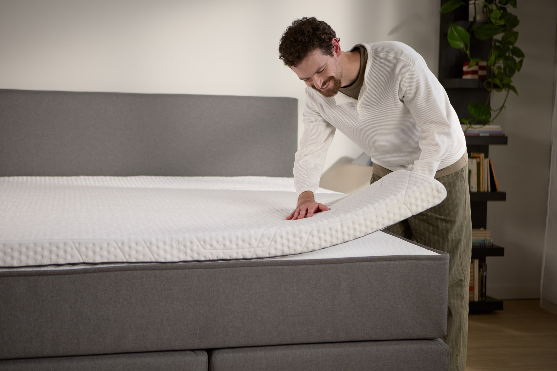 Detailansicht: Ein separater Matratzen-Topper wird auf dem Boxspringbett angehoben und zeigt die zusätzliche Polsterung an der Oberfläche.