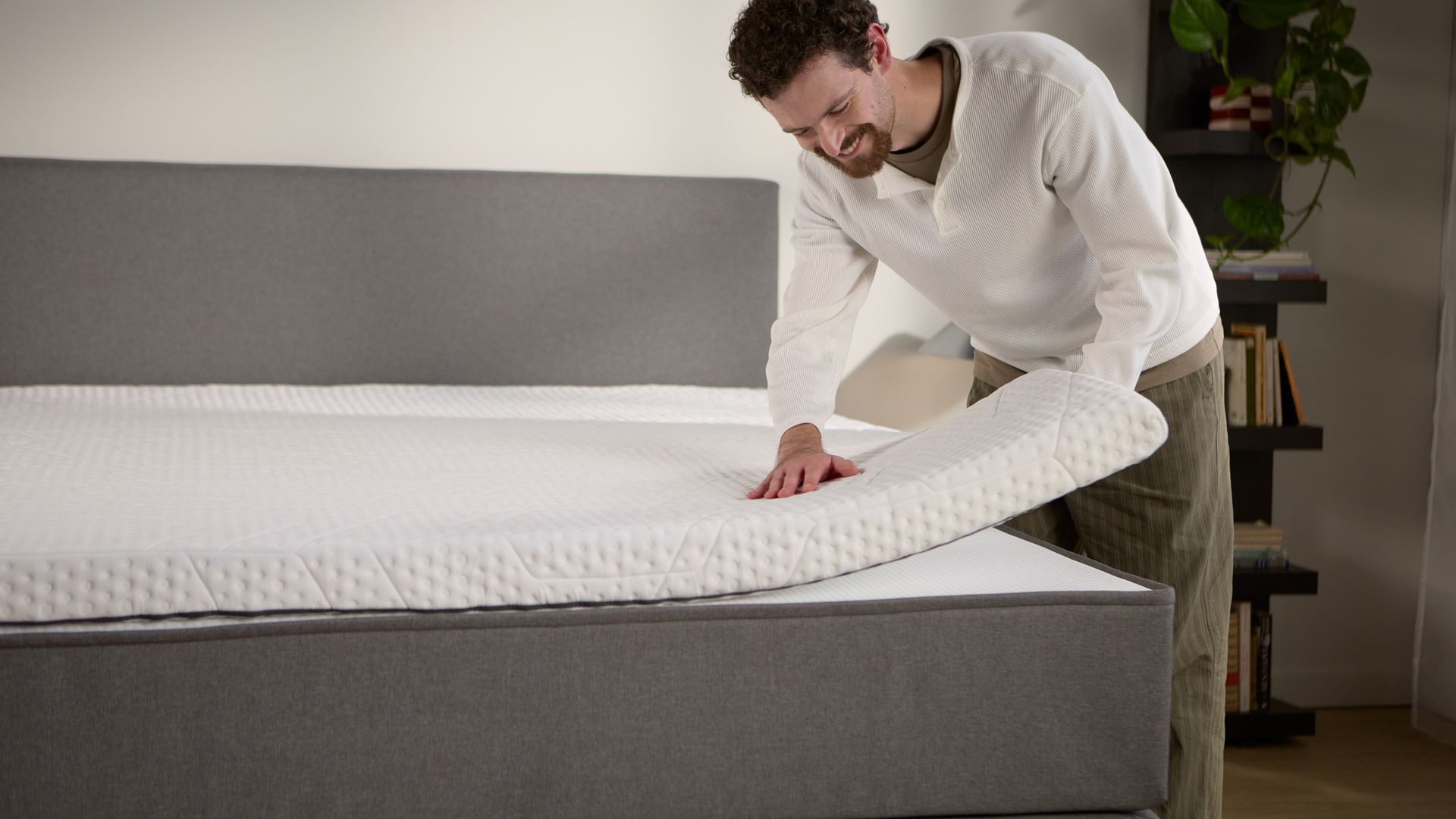 Detailansicht: Ein separater Matratzen-Topper wird auf dem Boxspringbett angehoben und zeigt die zusätzliche Polsterung an der Oberfläche.