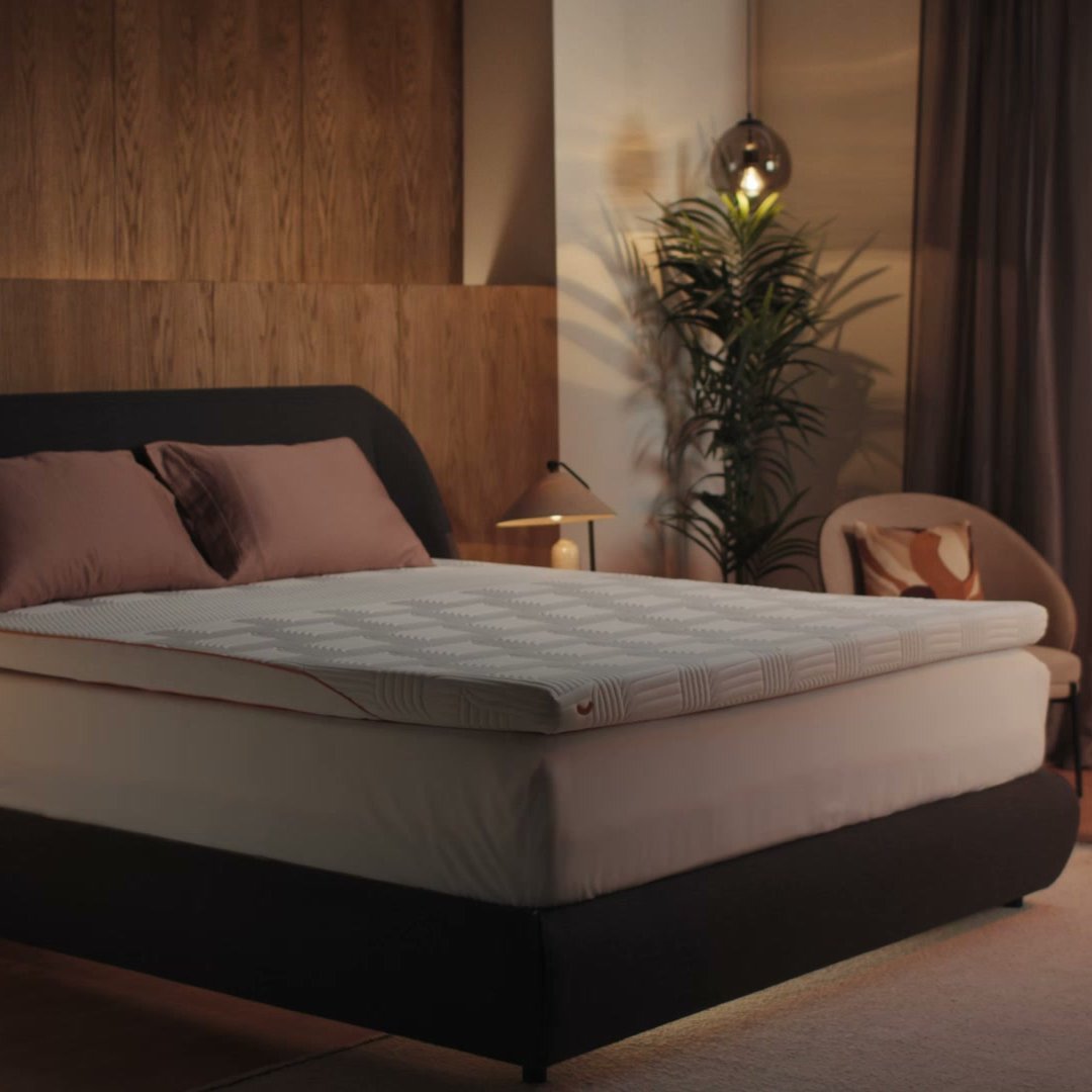 Man stretching by bedroom window at sunrise with Emma Performance Topper on dark boxspringbed.