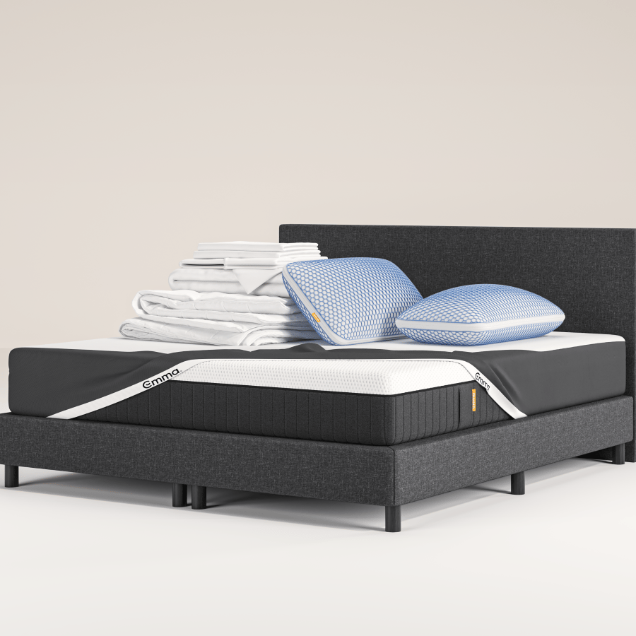 Un lit moderne avec un cadre et une tête de lit gris foncé, surmonté de deux oreillers bleus empilés, d'une literie blanche pliée et d'une couverture grise, se trouve sur un tapis clair dans une pièce bleue minimale, à côté d'une petite table d'appoint ronde.