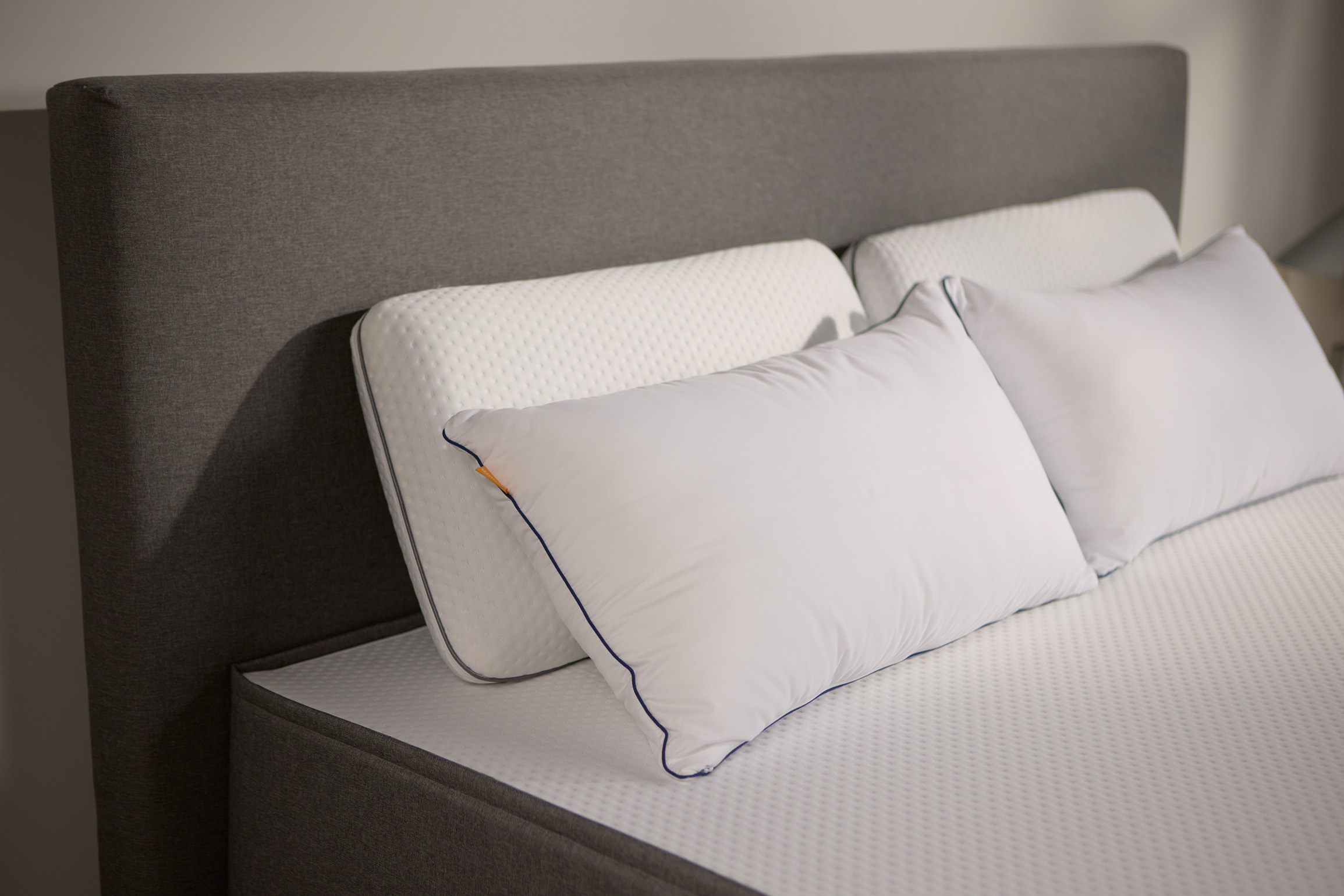 Close-up van het donkergrijs gestoffeerde bedframe, met twee paar Emma kussens van schuim en microvezel.