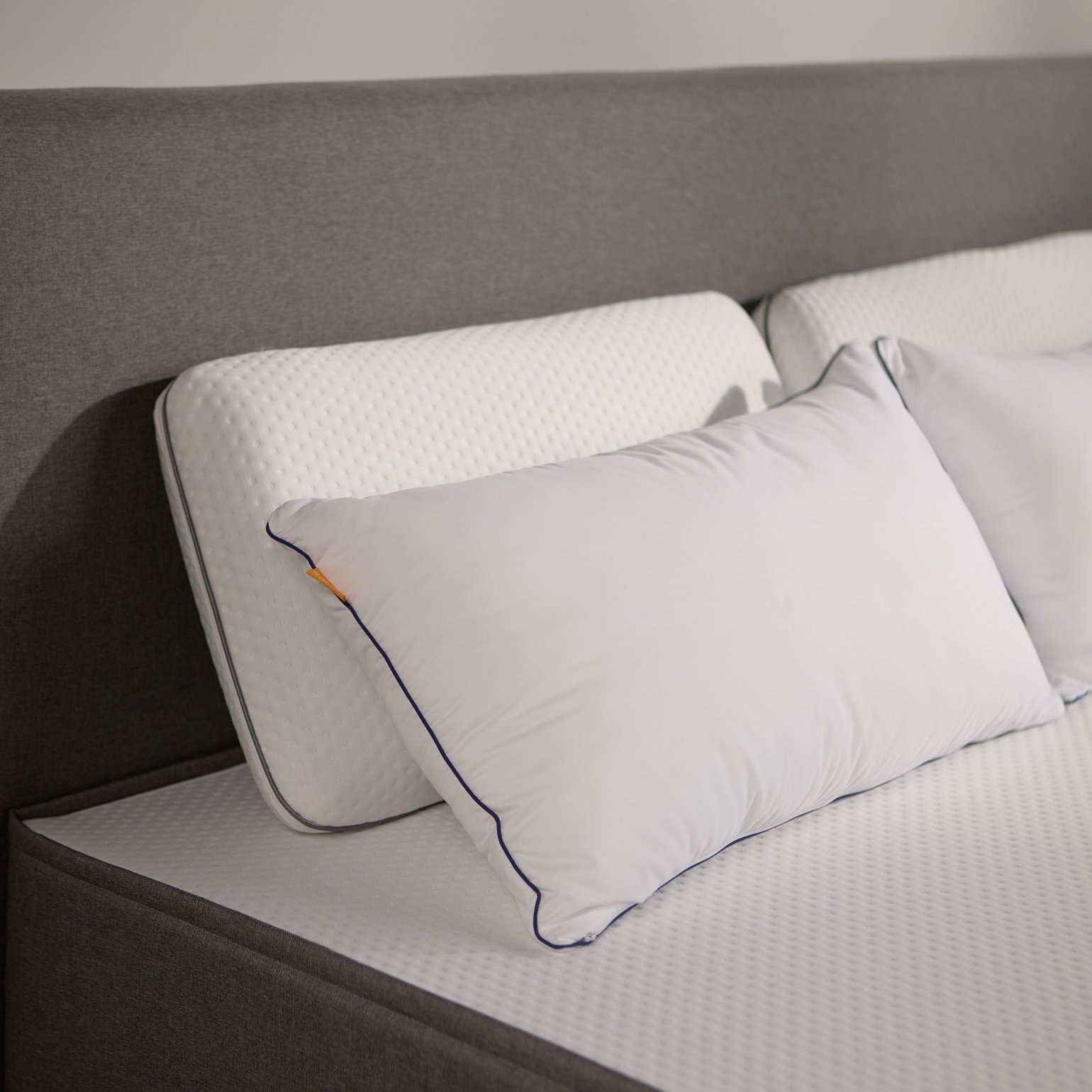 Close-up van het donkergrijs gestoffeerde bedframe, met twee paar Emma kussens van schuim en microvezel.