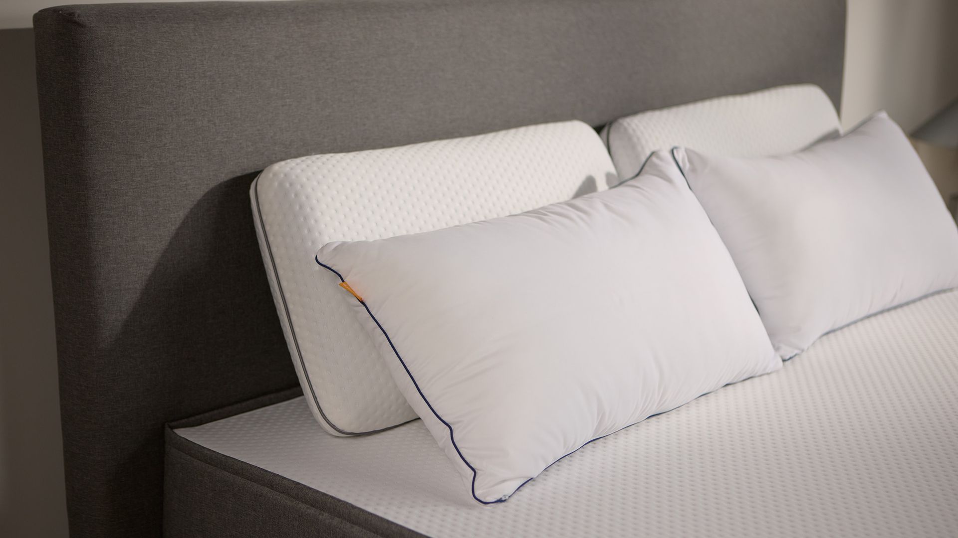 Close-up van het donkergrijs gestoffeerde bedframe, met twee paar Emma kussens van schuim en microvezel.