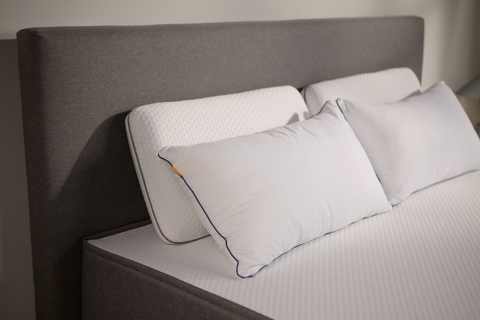Close-up van het donkergrijs gestoffeerde bedframe, met twee paar Emma kussens van schuim en microvezel.