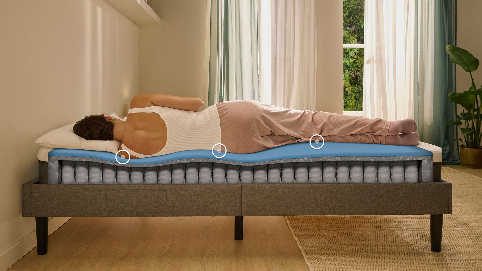 Woman sleeping on her side on an Emma Original Lite mattress with a layers view showing foam and spring construction beneath her.
