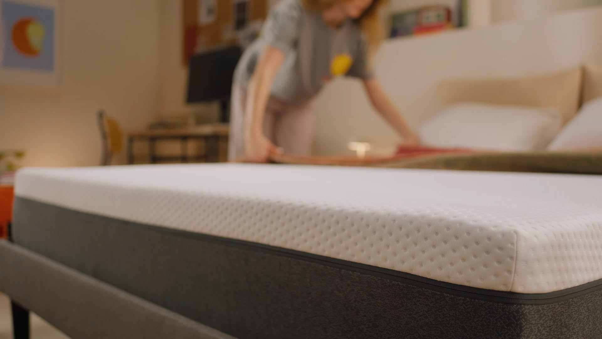 Person sitting on a bed with a white mattress in a bright bedroom.