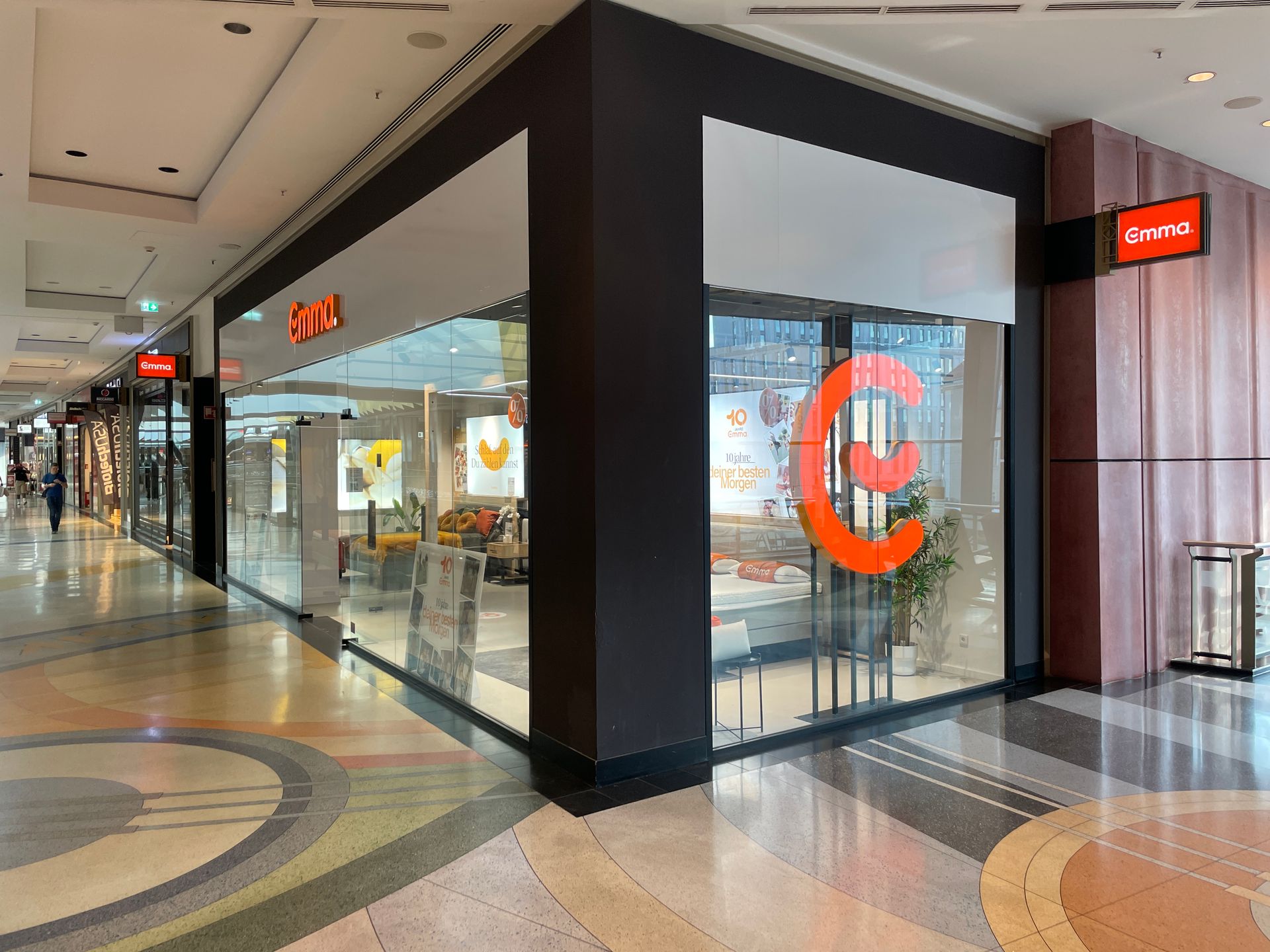 Emma Store Berlin – moderner Laden im Einkaufszentrum mit großen Glasfronten und orangefarbenem Emma-Logo.