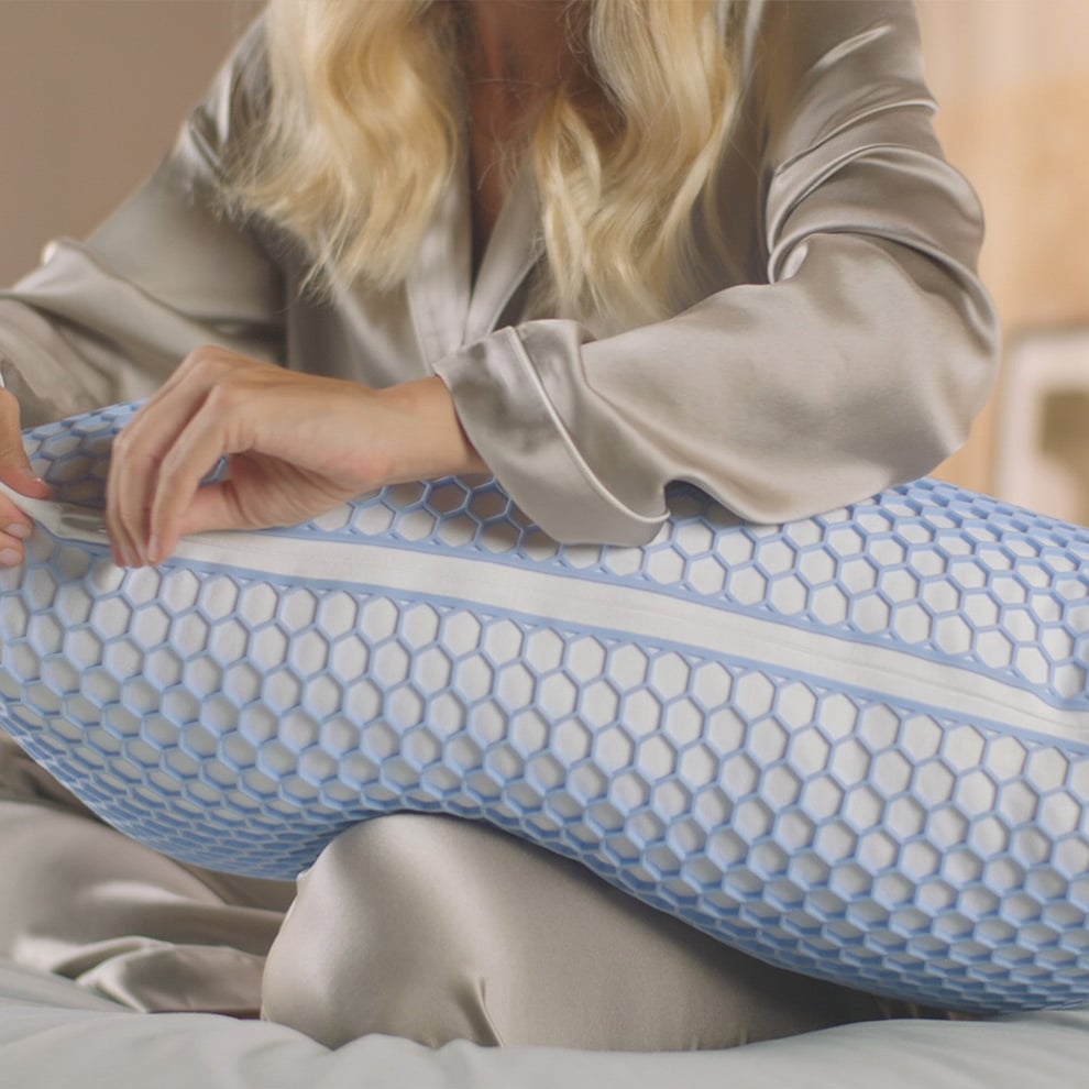 Imagem de uma mulher sentada em cima da sua cama, com uma Almofada Emma Original Microfibra Elite ao seu colo, a sentir a sua firmeza