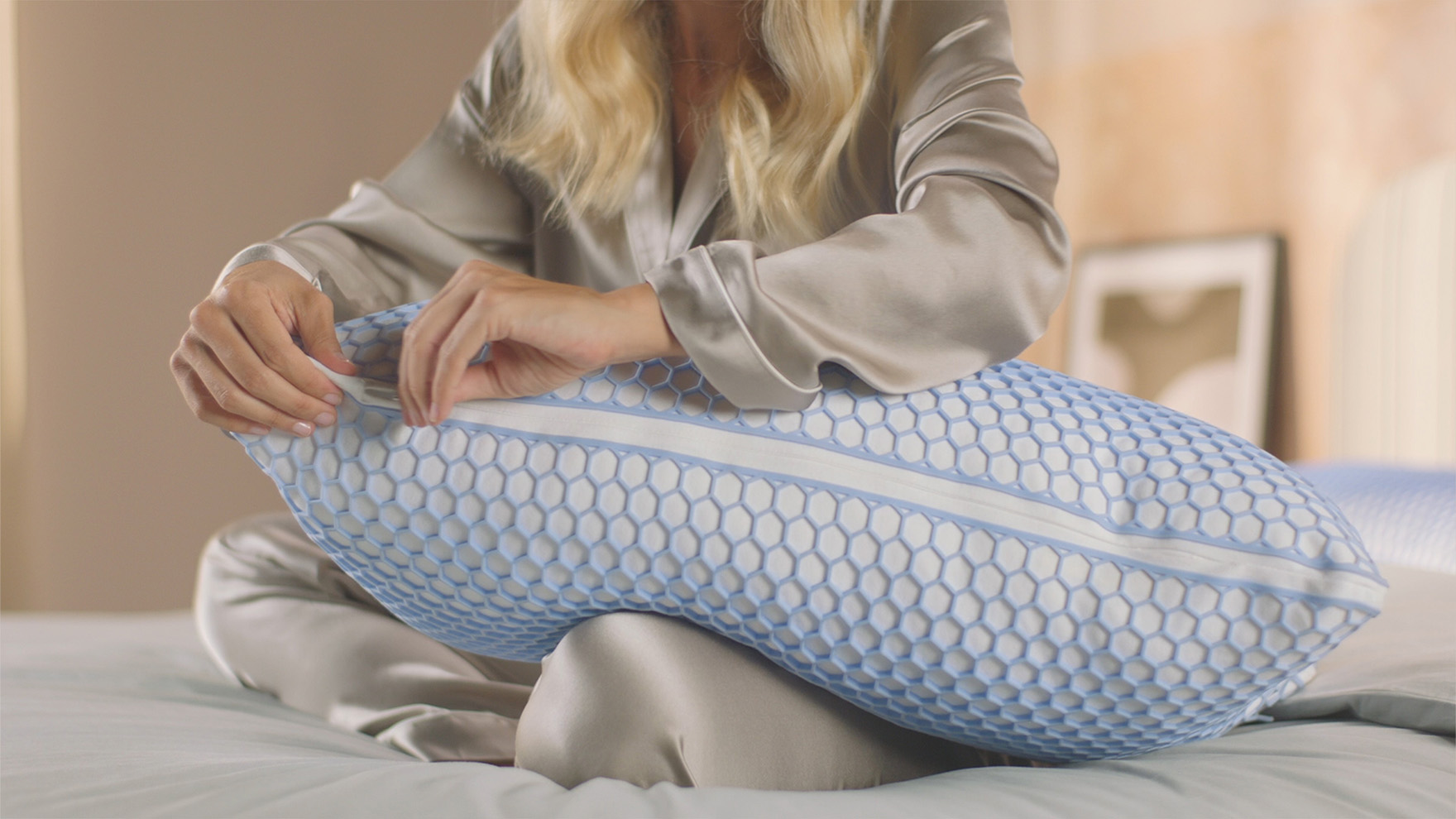 Imagem de uma mulher sentada em cima da sua cama, com uma Almofada Emma Original Microfibra Elite ao seu colo, a sentir a sua firmeza