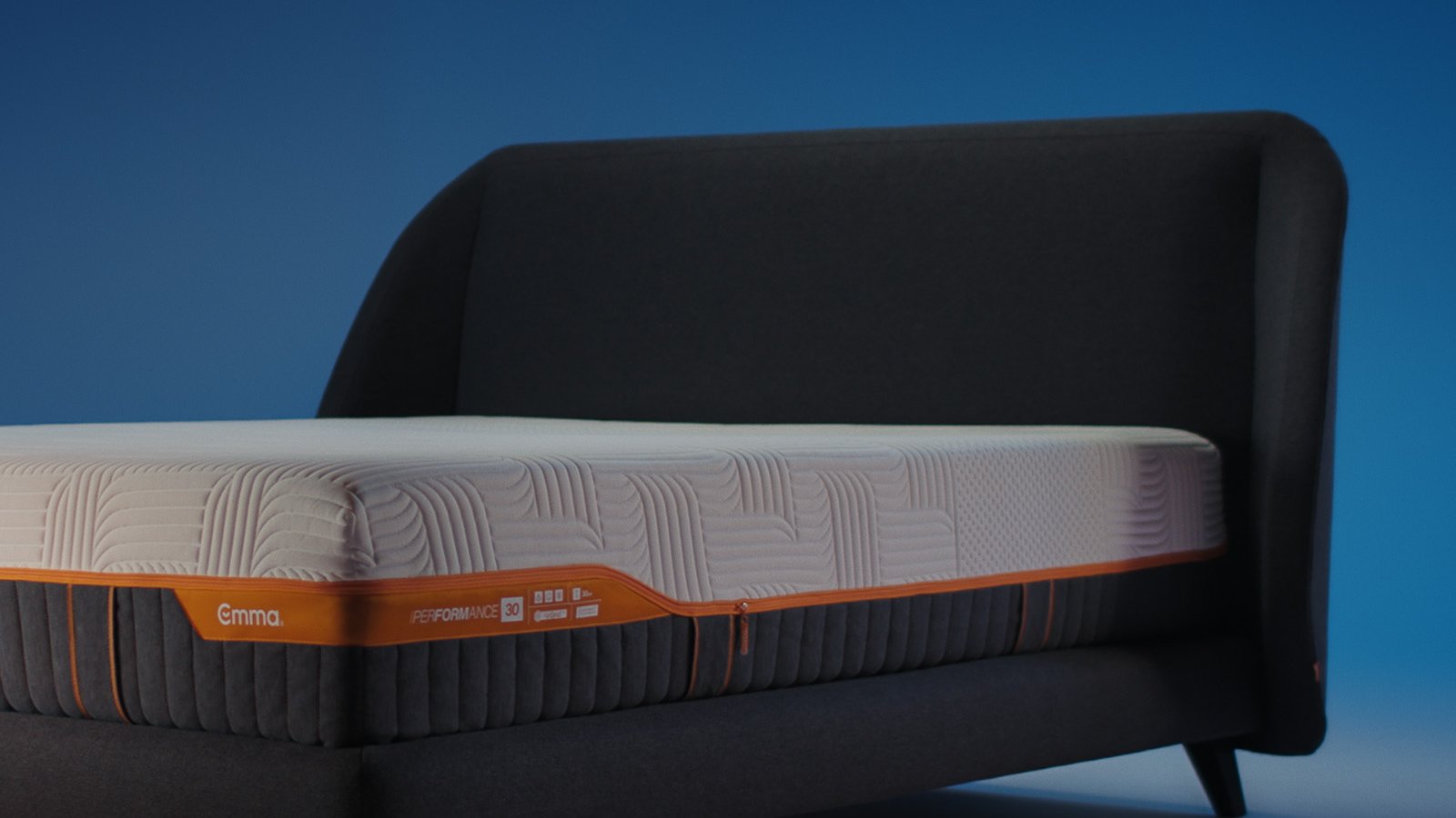 Emma Performance boxspringbed with charcoal upholstered curved headboard, matching base, and black tapered legs.