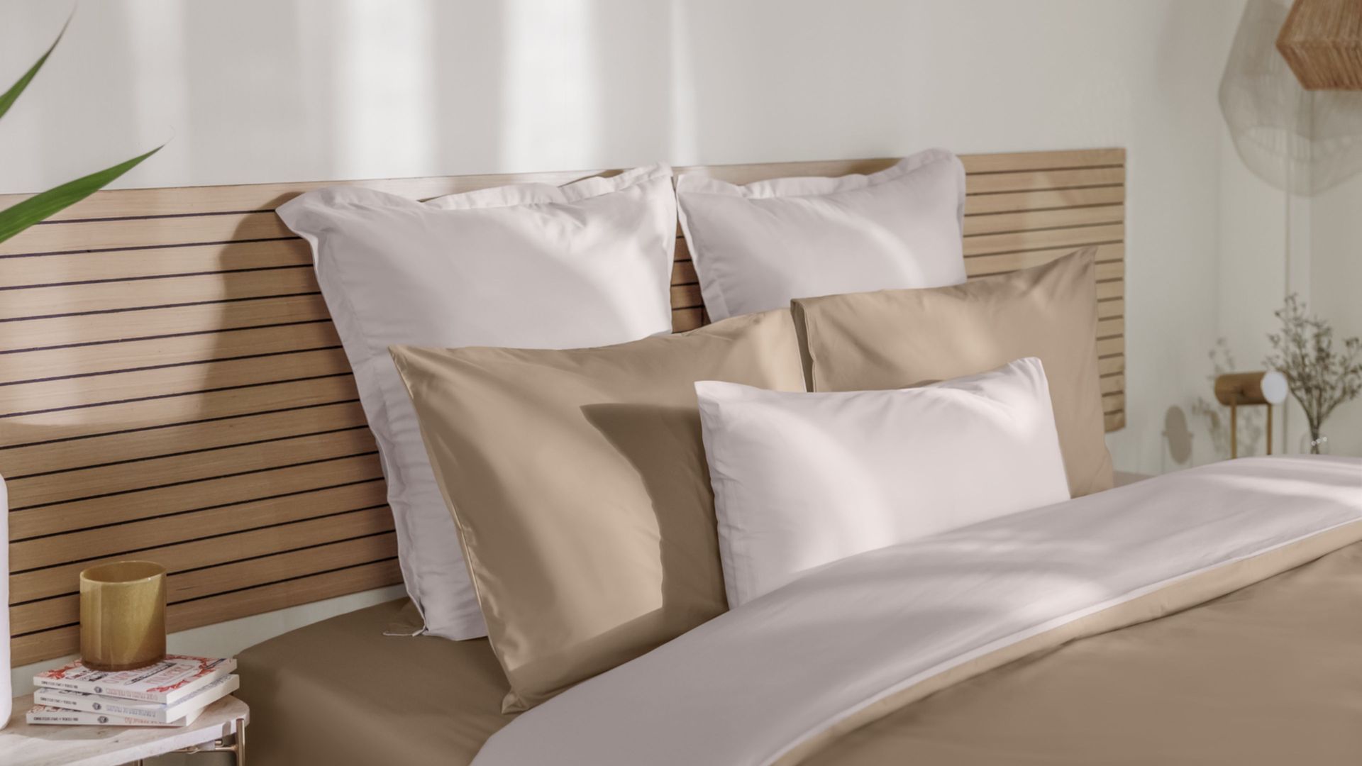 Letto con federe beige e bianche, coperta coordinata e testiera in legno.