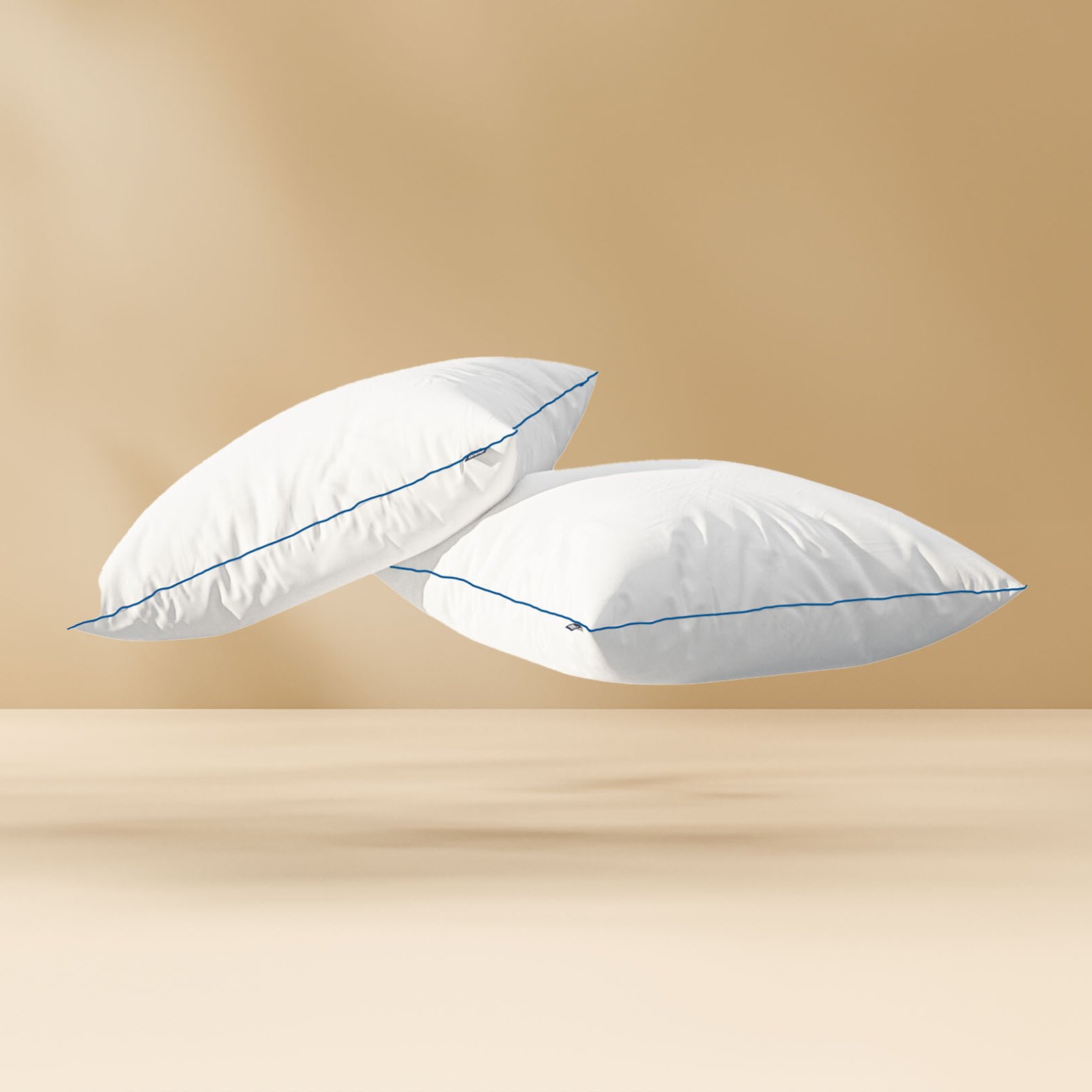 Deux Oreillers Nuage blancs avec passepoil bleu, flottant sur fond beige.