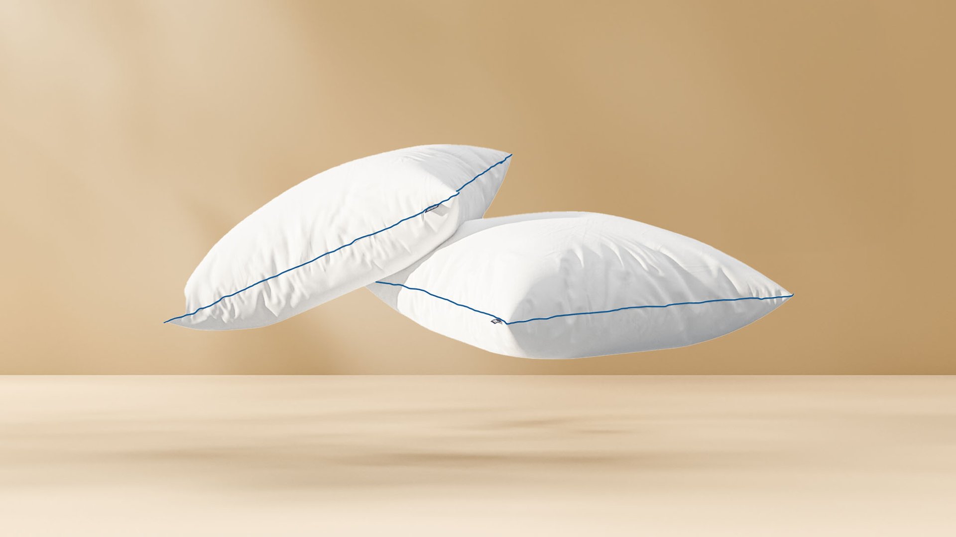 Deux Oreillers Nuage blancs avec passepoil bleu, flottant sur fond beige.