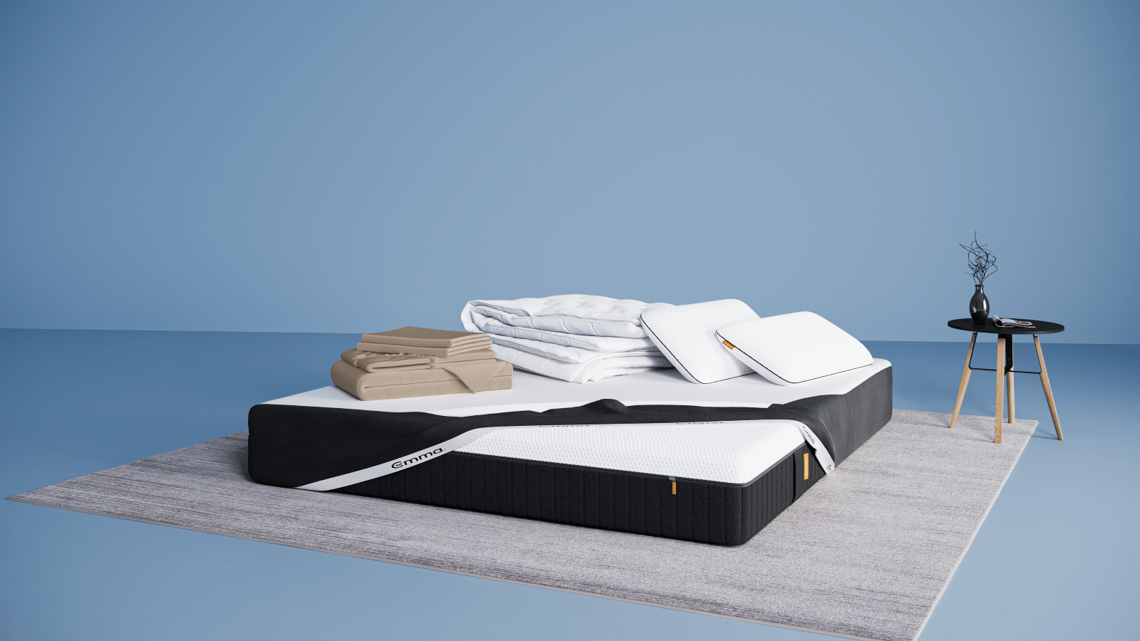 Ensemble de literie présenté dans une chambre moderne : matelas Hybride II ou Hybride Premium II avec base noire et surface blanche, partiellement recouvert d’un plaid gris foncé. Sur le matelas, deux oreillers Nuage Elite 40x70 cm bleus, une couette Nuage Tempérée blanche pliée, un protège-matelas, et une parure de lit en satin de coton blanc comprenant une housse de couette et des taies d’oreillers. Le tout est posé sur un tapis clair, avec une table d’appoint noire à pieds en bois et une décoration minimaliste.