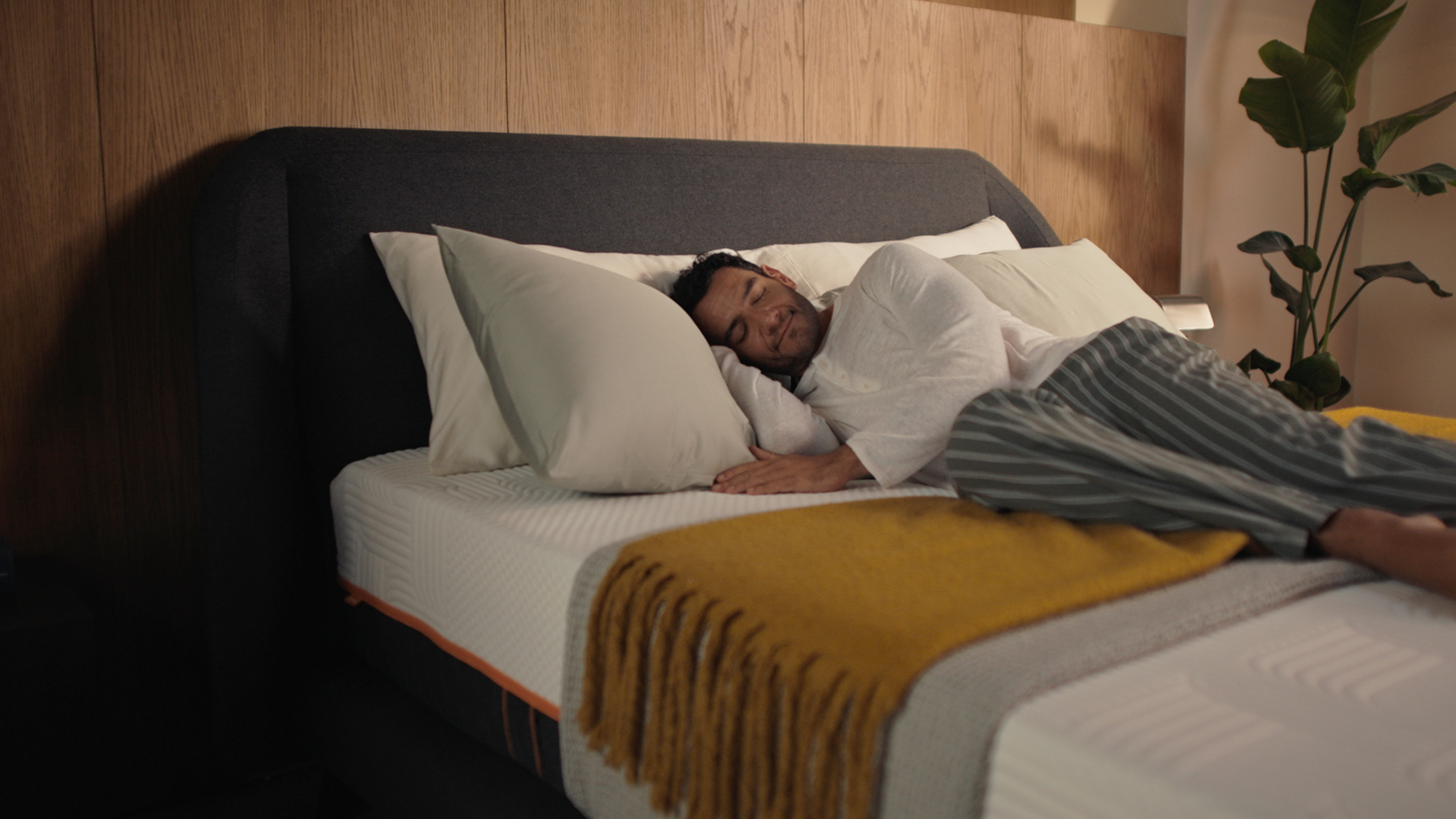 Man sleeping on Emma Performance boxspringbed with charcoal upholstered headboard in a warm, styled bedroom.