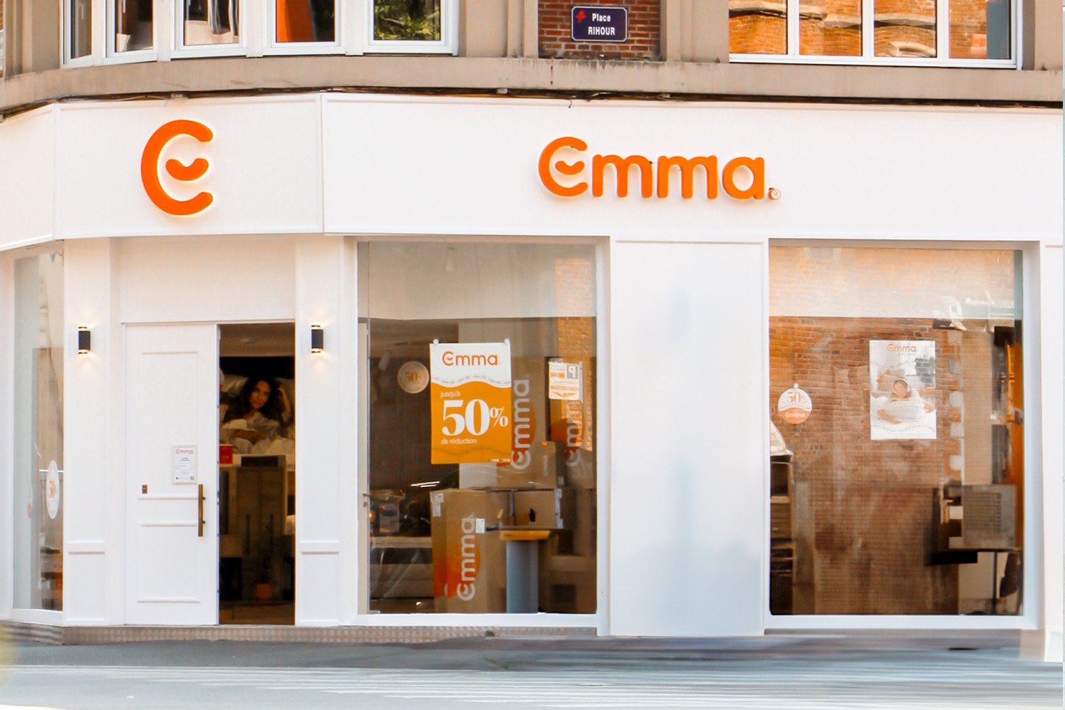 Façade du magasin physique Emma, avec le logo Emma en orange et une affiche promotionnelle dans la vitrine.