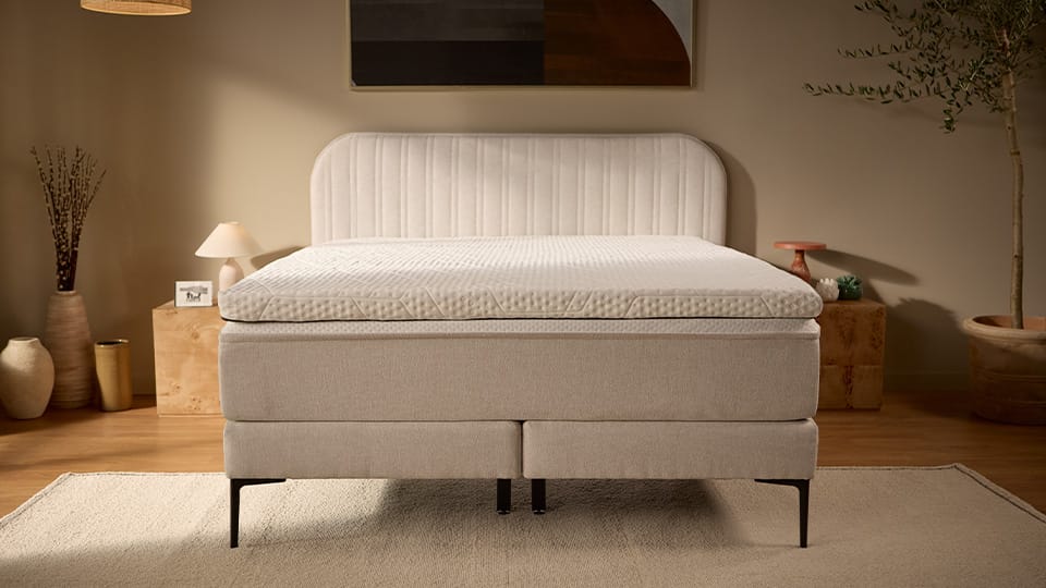 Beige upholstered bed with white mattress and slim black legs.