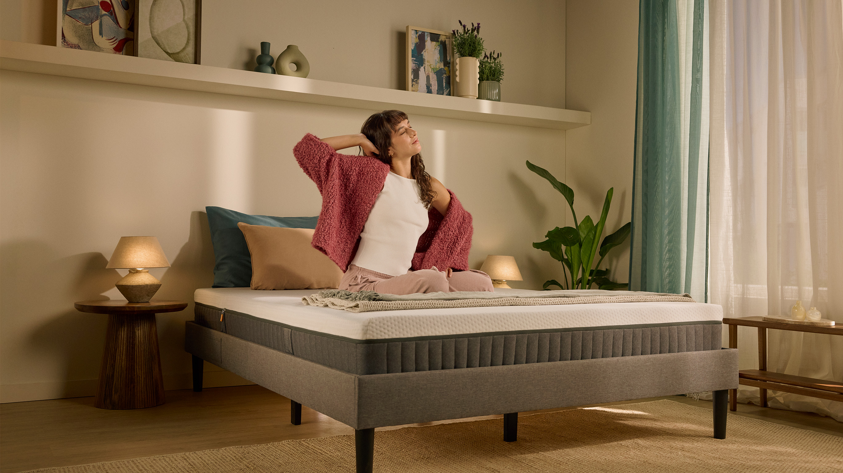 Person sitting up on a bed with a white mattress in the morning.