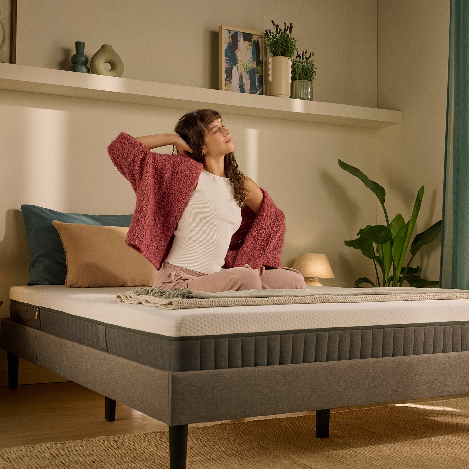 Person sitting up on a bed with a white mattress in the morning.