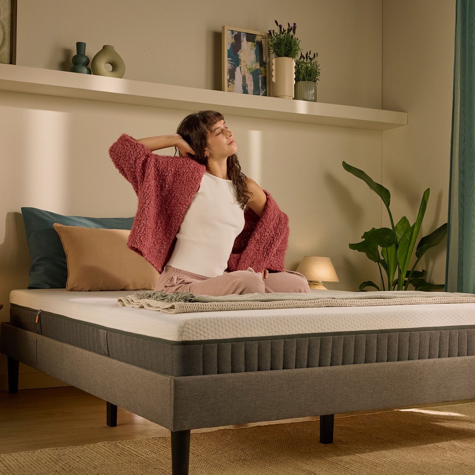 Une personne assise sur un lit au matelas blanc, le matin.
