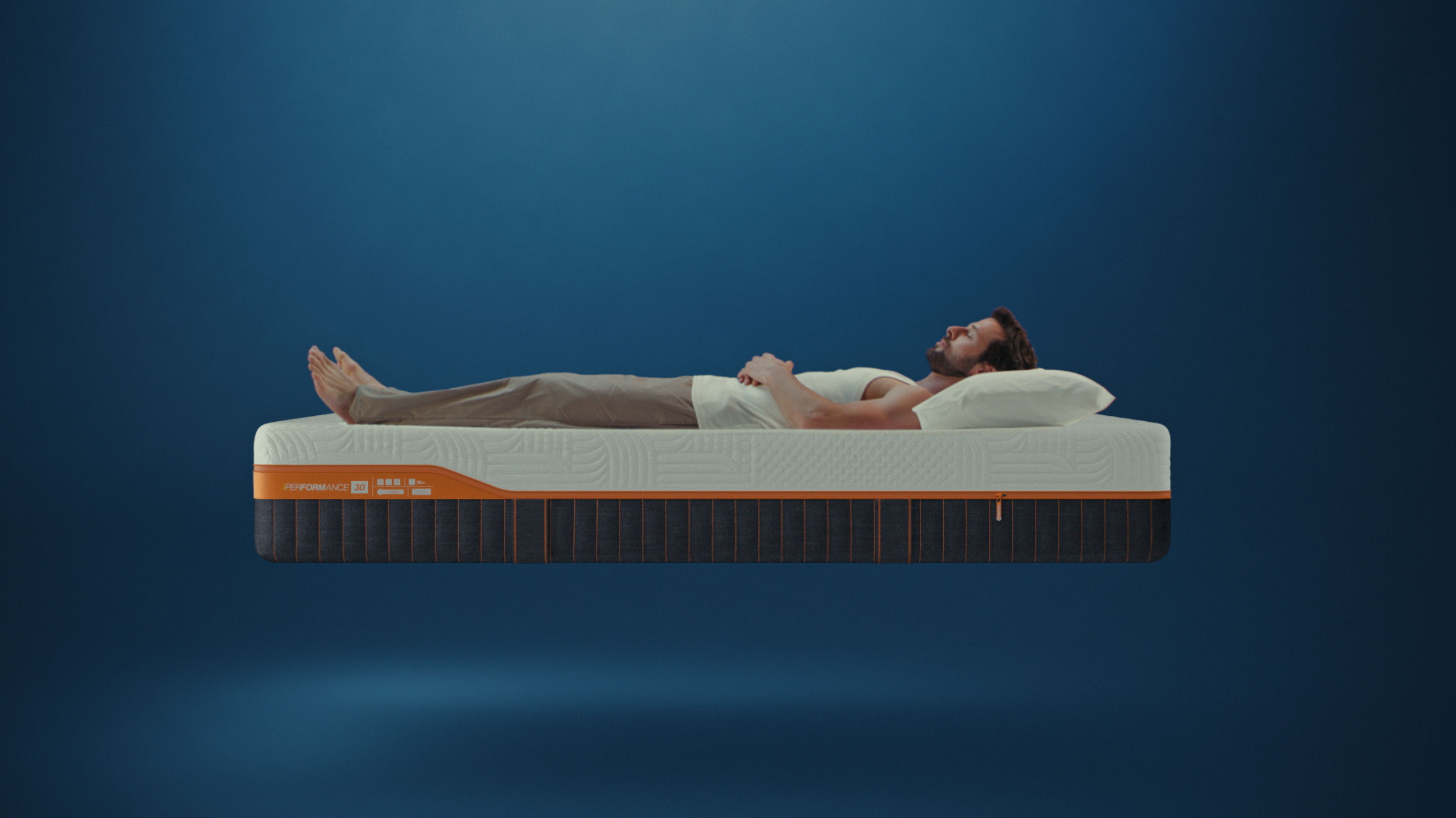 Man lying on Emma Performance mattress with textured white cover and dark base with orange trim.