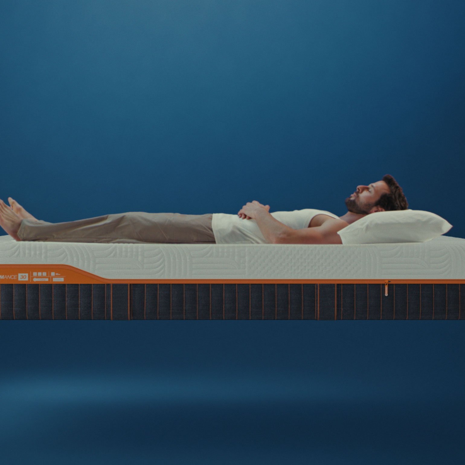 Man lying on Emma Performance mattress with textured white cover and dark base with orange trim.