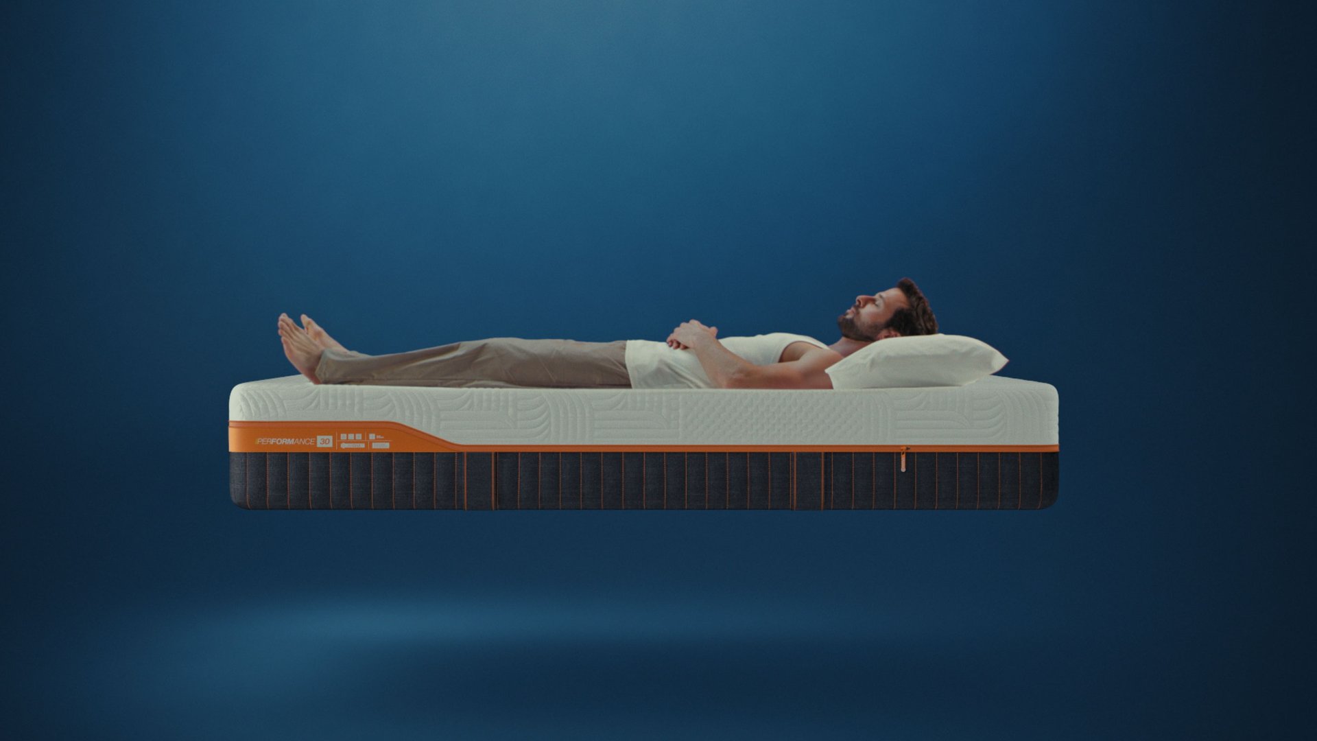 Man lying on Emma Performance mattress with textured white cover and dark base with orange trim.