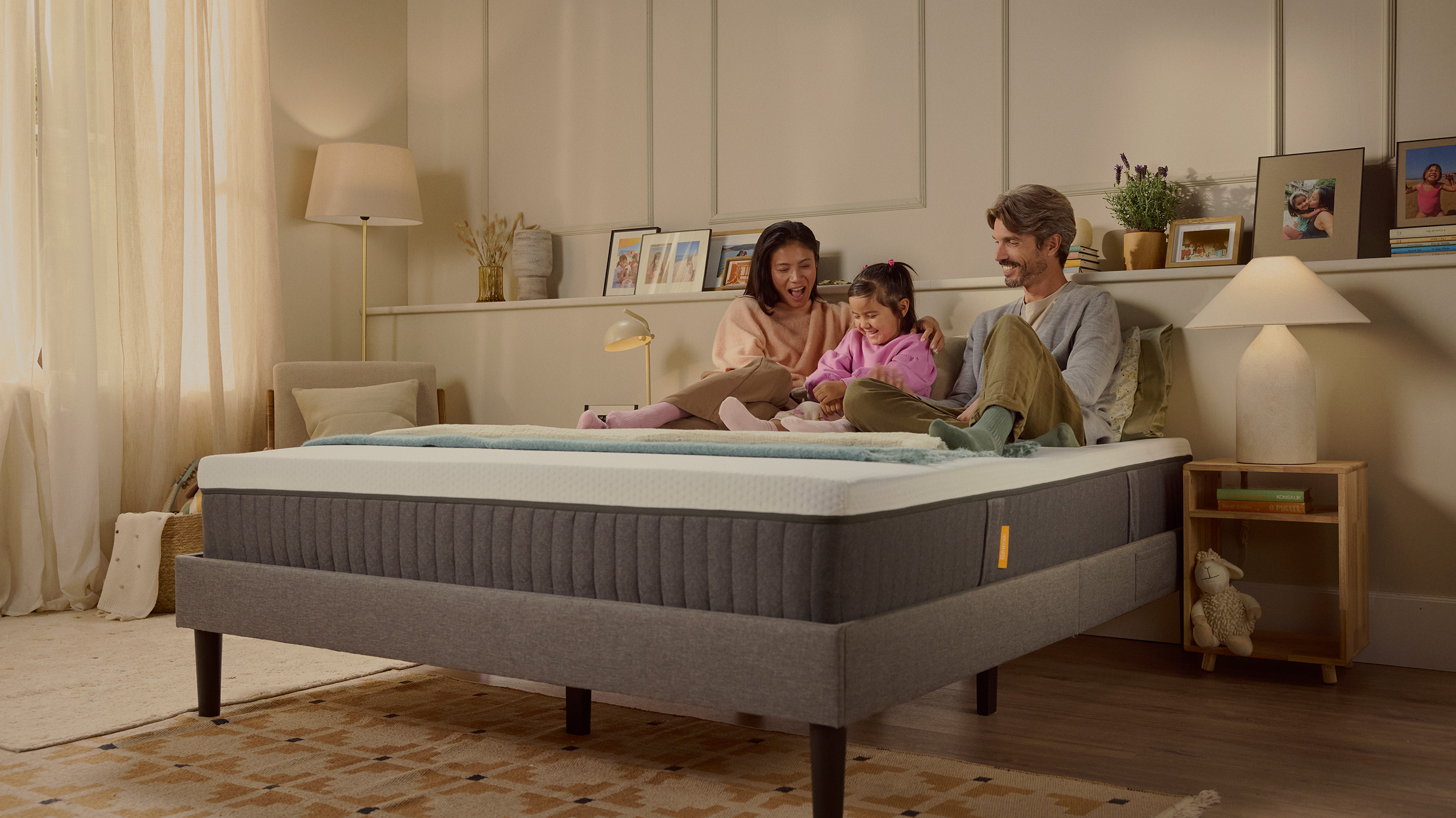 Famille assise ensemble sur un lit dans une chambre chaleureuse, mettant en valeur le confort et la stabilité d’un matelas moderne au design premium. La scène illustre une atmosphère cosy et conviviale.
