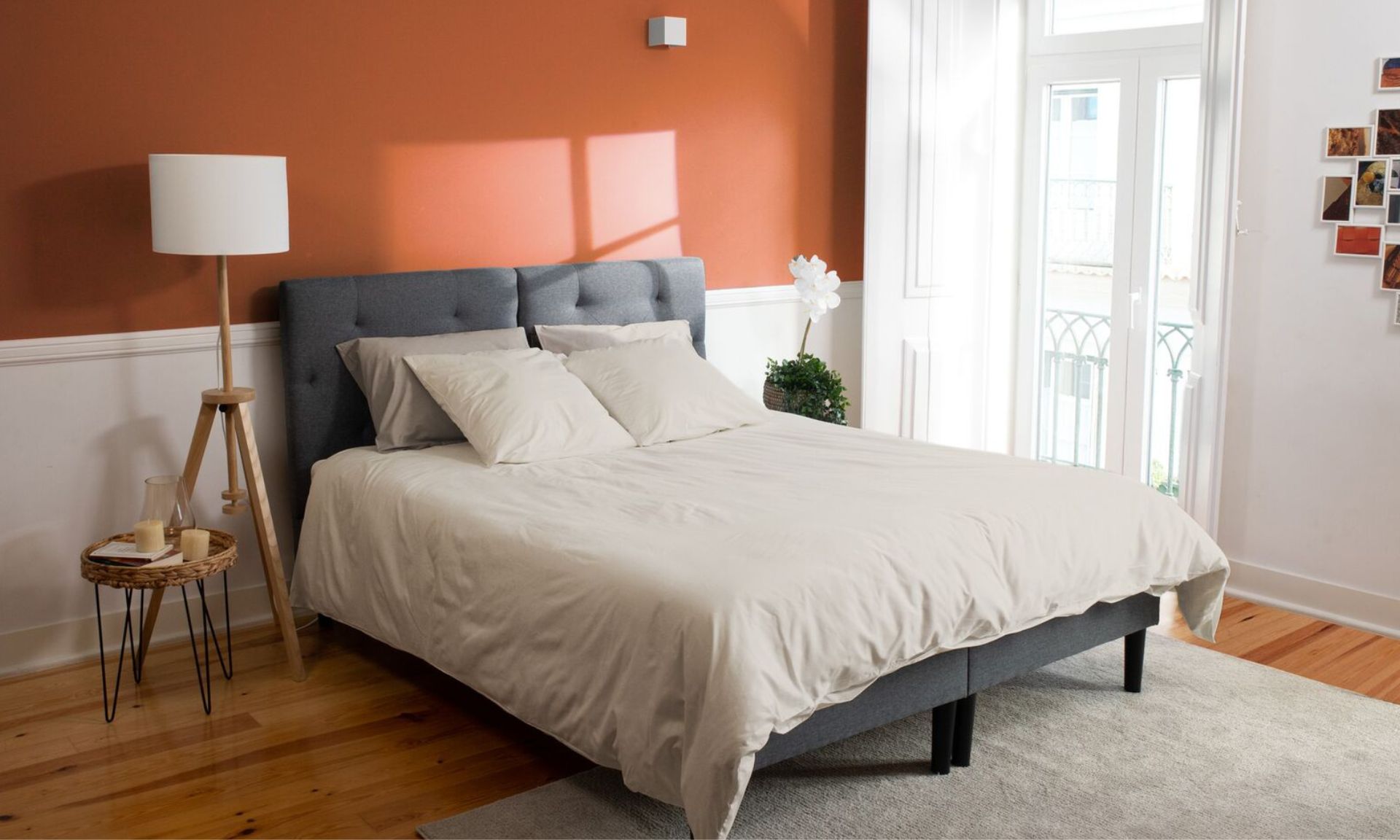 Camera da letto ordinata con parete arancione, letto con testiera grigia e decorazioni naturali.