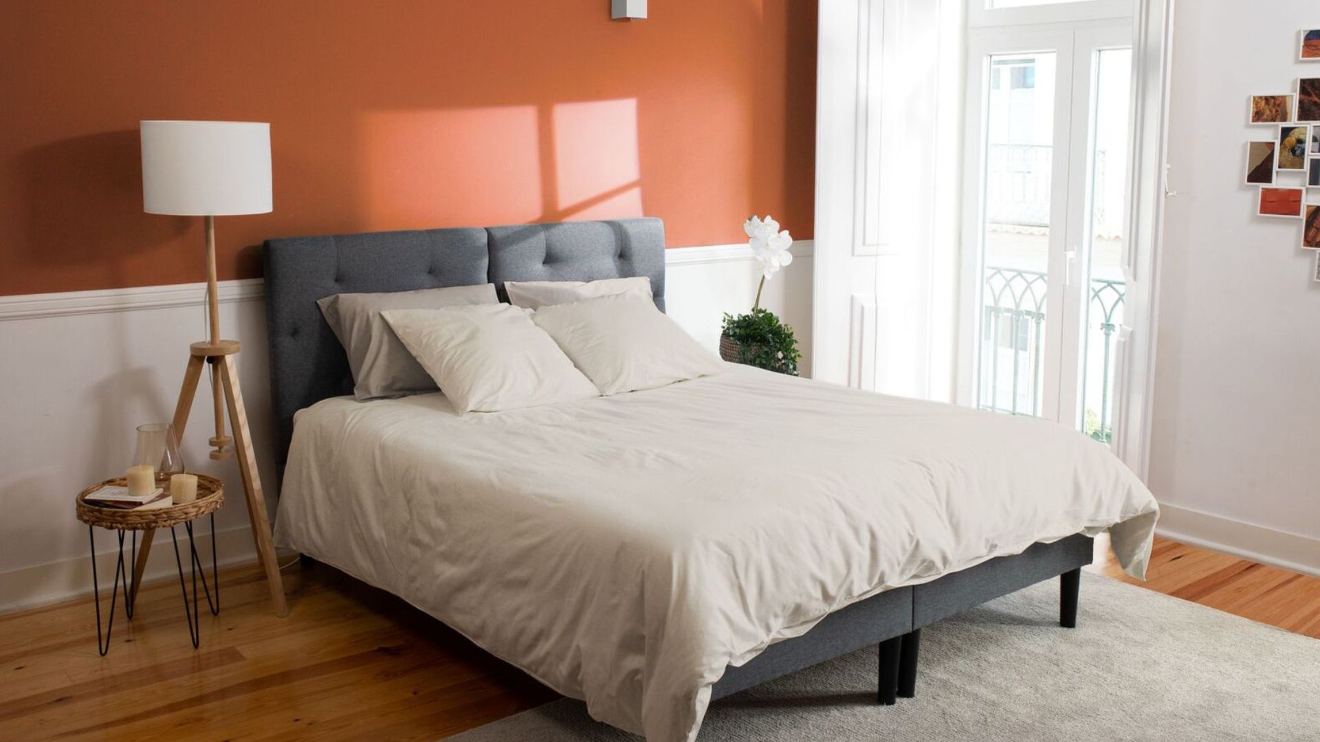 Camera da letto ordinata con parete arancione, letto con testiera grigia e decorazioni naturali.