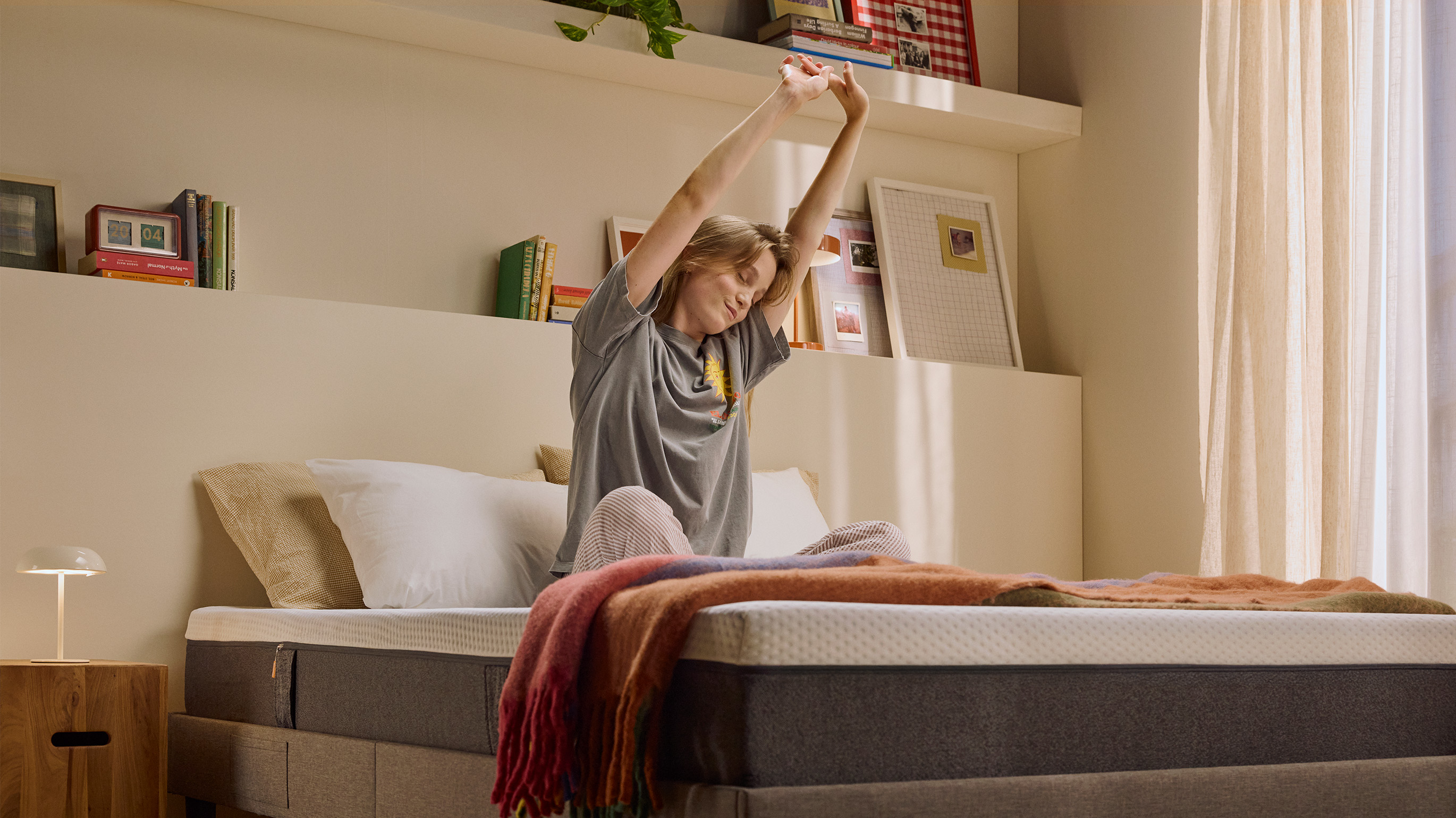 Person sitting up on a bed with a white mattress in the morning.