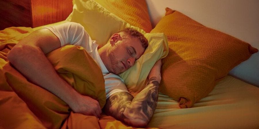 Chico rubio durmiendo con ropa de cama naranja y amarilla