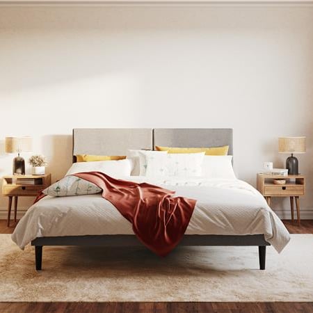 Chambre confortable avec un lit blanc, une tête de lit grise, un plaid rouge, des tables de chevet en bois, un tapis beige et un arbre en pot, baignée de lumière naturelle.
