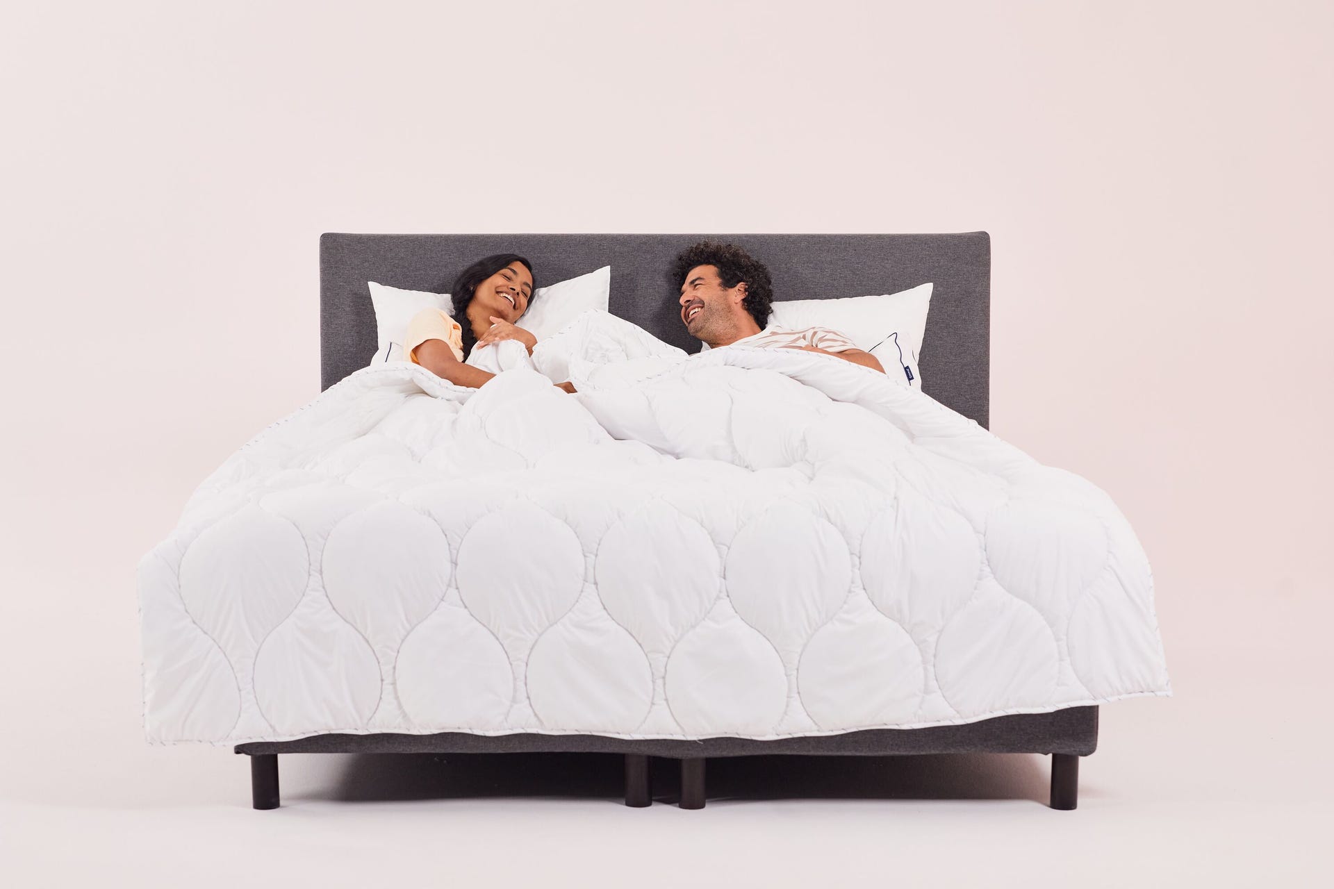 pareja riendo en la cama arropados con un edredón blanco