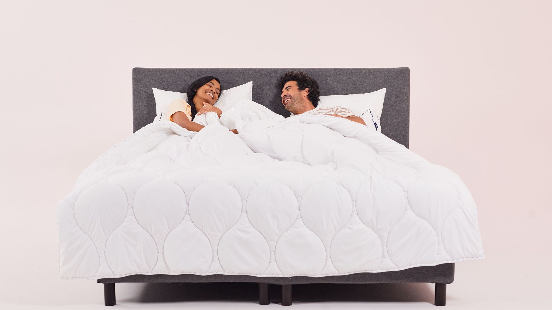 pareja riendo en la cama arropados con un edredón blanco