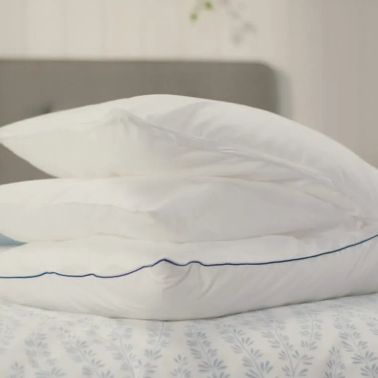 Original Cooling Comfort Kussen op bed om alle verwijderbare lagen te zien. Op de achtergrond staat een grijs gestoffeerd hoofdbord en een gele lamp op een nachtkastje. Deze afbeelding toont het luchtige en stijlvolle ontwerp van het Emma Wolkenkussen in een huiselijke setting.
