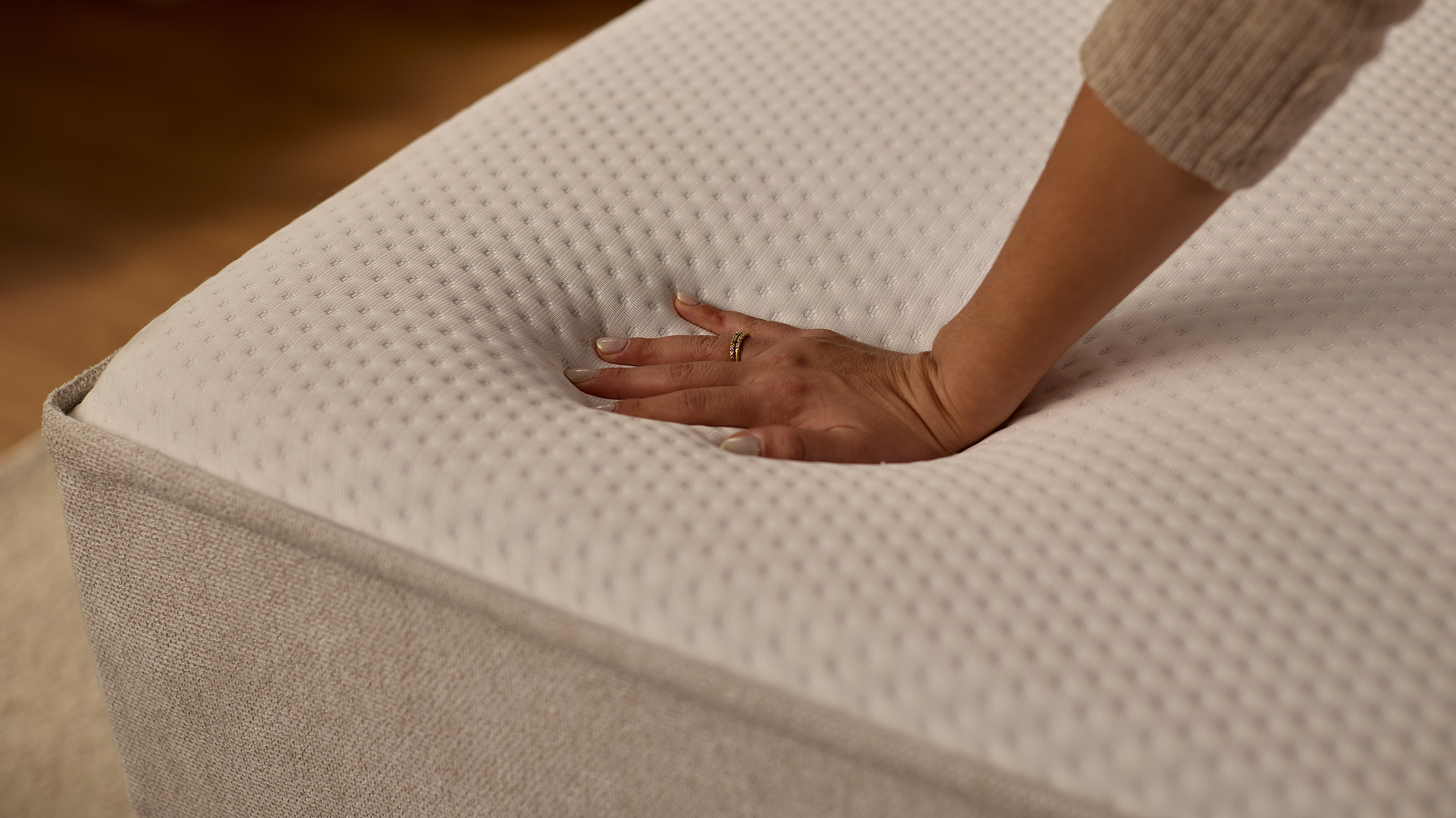 Hand pressing into the surface of the Emma Boxspring Bed mattress top, showing softness and responsiveness in close-up detail.