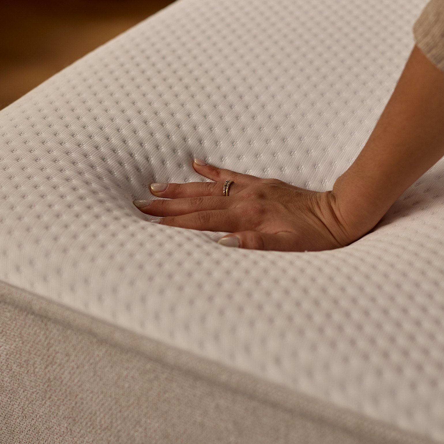 Hand pressing into the surface of the Emma Boxspring Bed mattress top, showing softness and responsiveness in close-up detail.