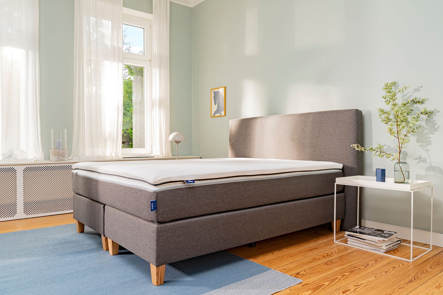 Graues Boxspringbett mit Holzfüßen und Topper im Schlafzimmer.