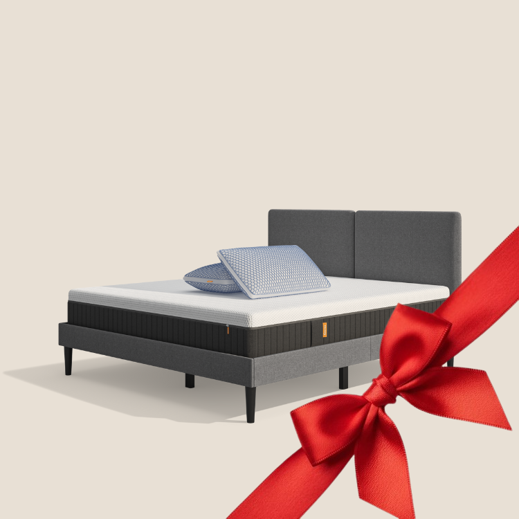 Lit moderne avec tête de lit grise et pieds noirs, recouvert de draps blancs. Deux oreillers blancs et une pile de linge plié sont posés sur le matelas. Arrière-plan beige avec une forme orange abstraite.