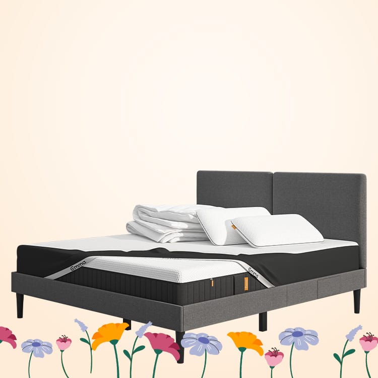 Lit moderne avec tête de lit grise et pieds noirs, recouvert de draps blancs. Deux oreillers blancs et une pile de linge plié sont posés sur le matelas. Arrière-plan beige avec une forme orange abstraite.