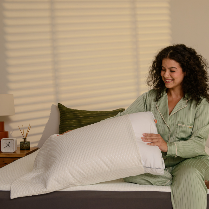 Pessoa sentada na cama a colocar um protetor de travesseiro em um travesseiro