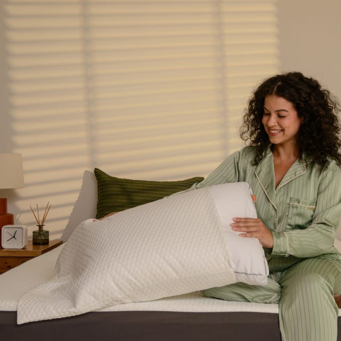 Pessoa sentada na cama a colocar um protetor de travesseiro em um travesseiro