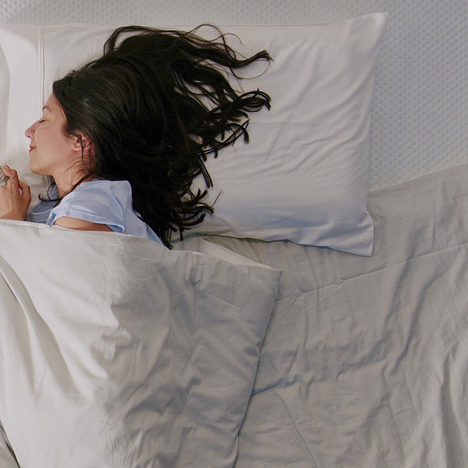 Frau schläft seitlich auf Matratze mit weißer Bettwäsche