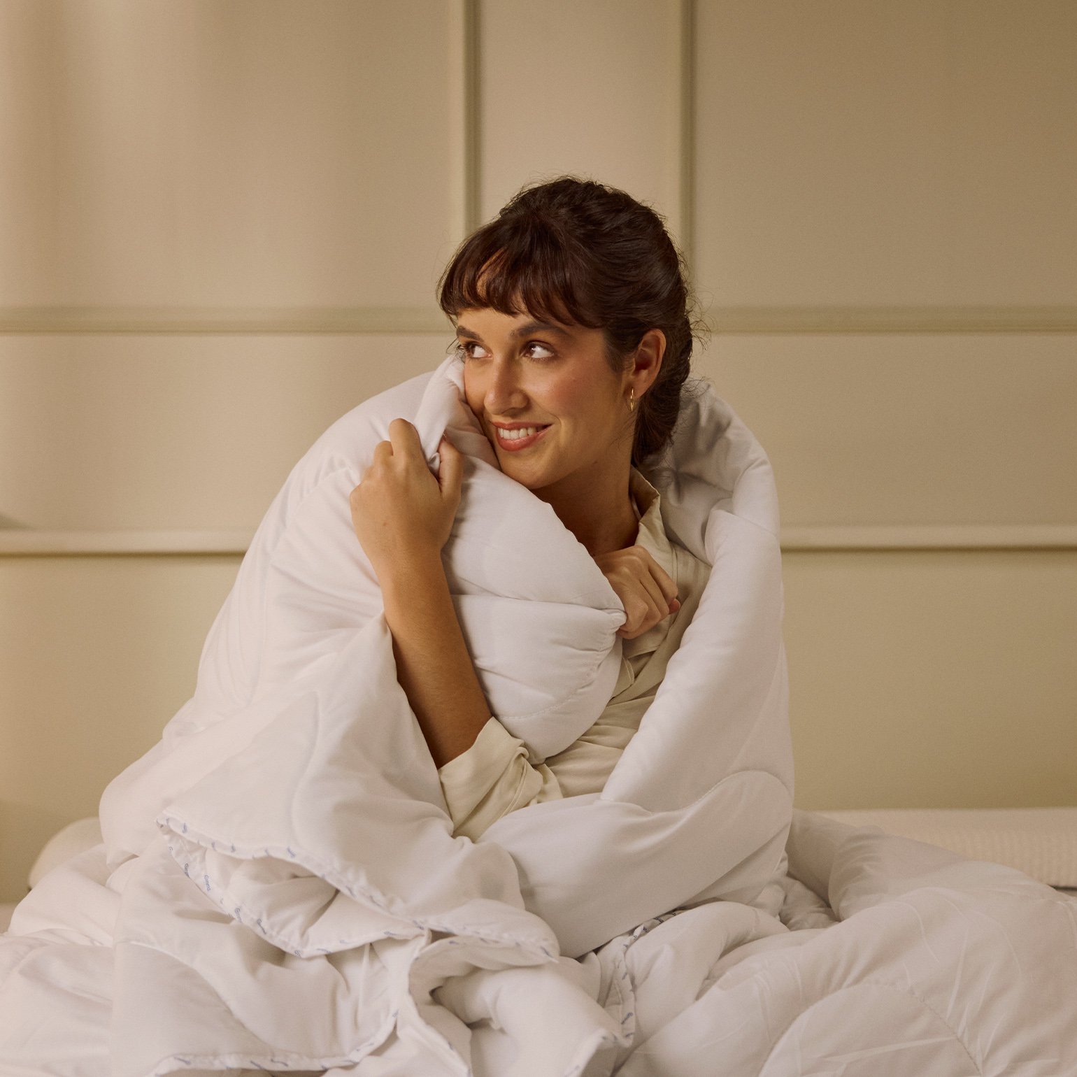 Person sitting on a bed, covered with a duvet.