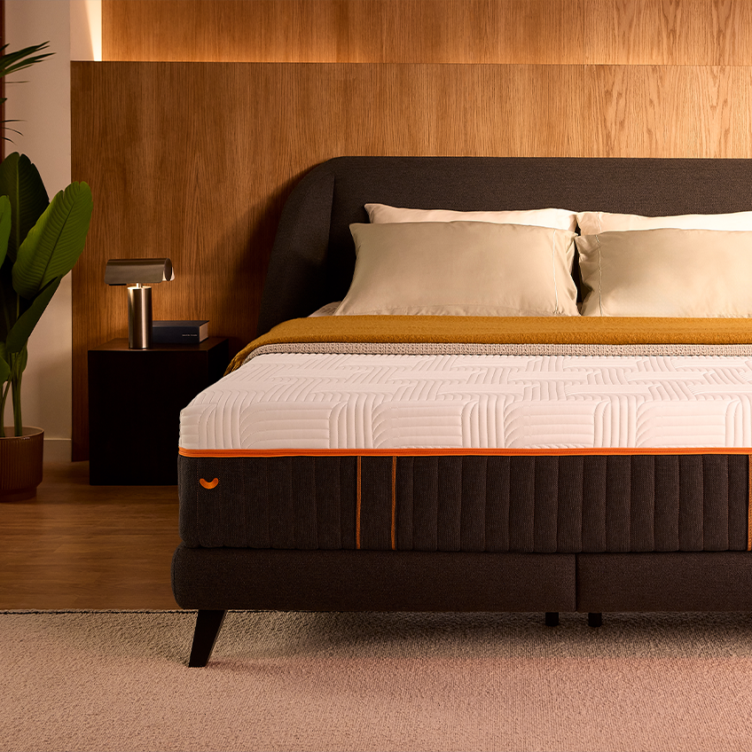 Front view of the Performance box spring bed dressed with pillows and a mustard throw in a warm wood-panelled bedroom