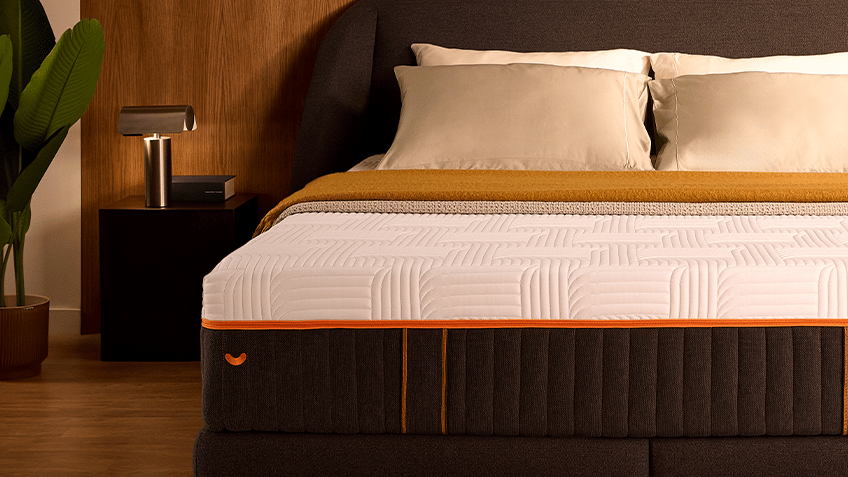Front view of the Performance box spring bed dressed with pillows and a mustard throw in a warm wood-panelled bedroom